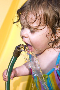 a toddler drinking water from a garden hose